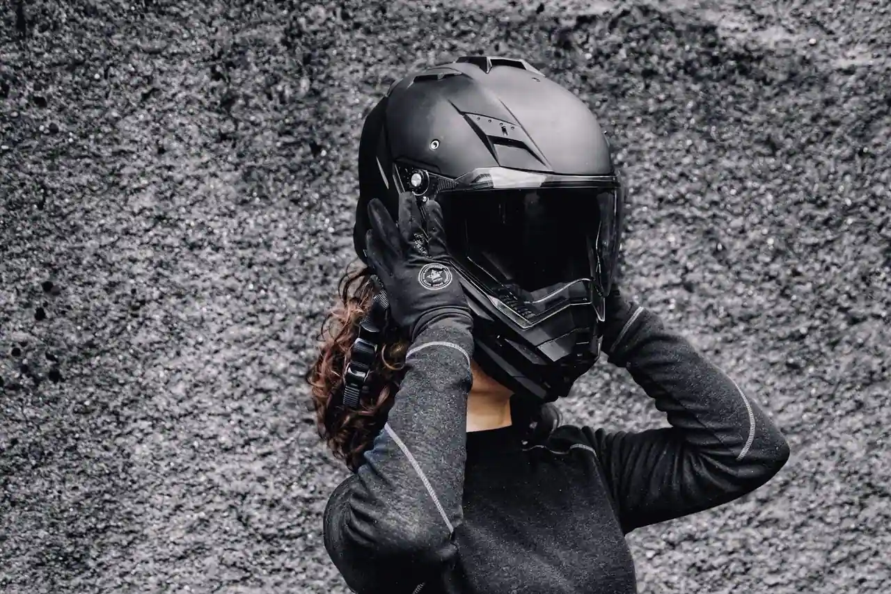 Motard ajustant son casque de moto intégral noir avec ses mains gantées, devant un mur gris