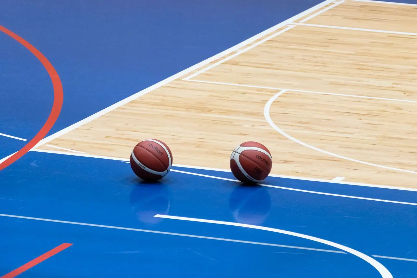 Deux ballons de basket posés sur le parquet d'un terrain couvert, ambiance de salle de match
