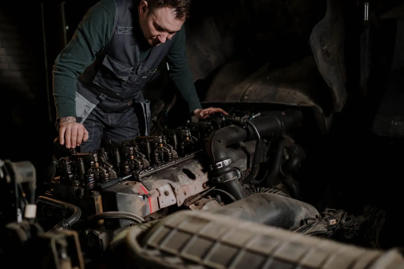 Mécanicien penché sur un gros moteur dans l'atelier sombre d'un garage automobile