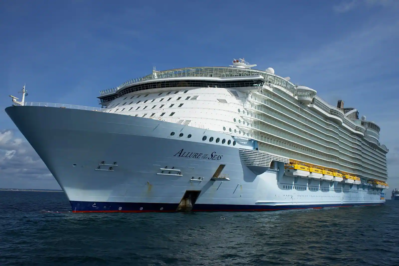 Grand bateau de croisière blanc naviguant sur une mer calme, vu de trois quarts sous un ciel dégagé.