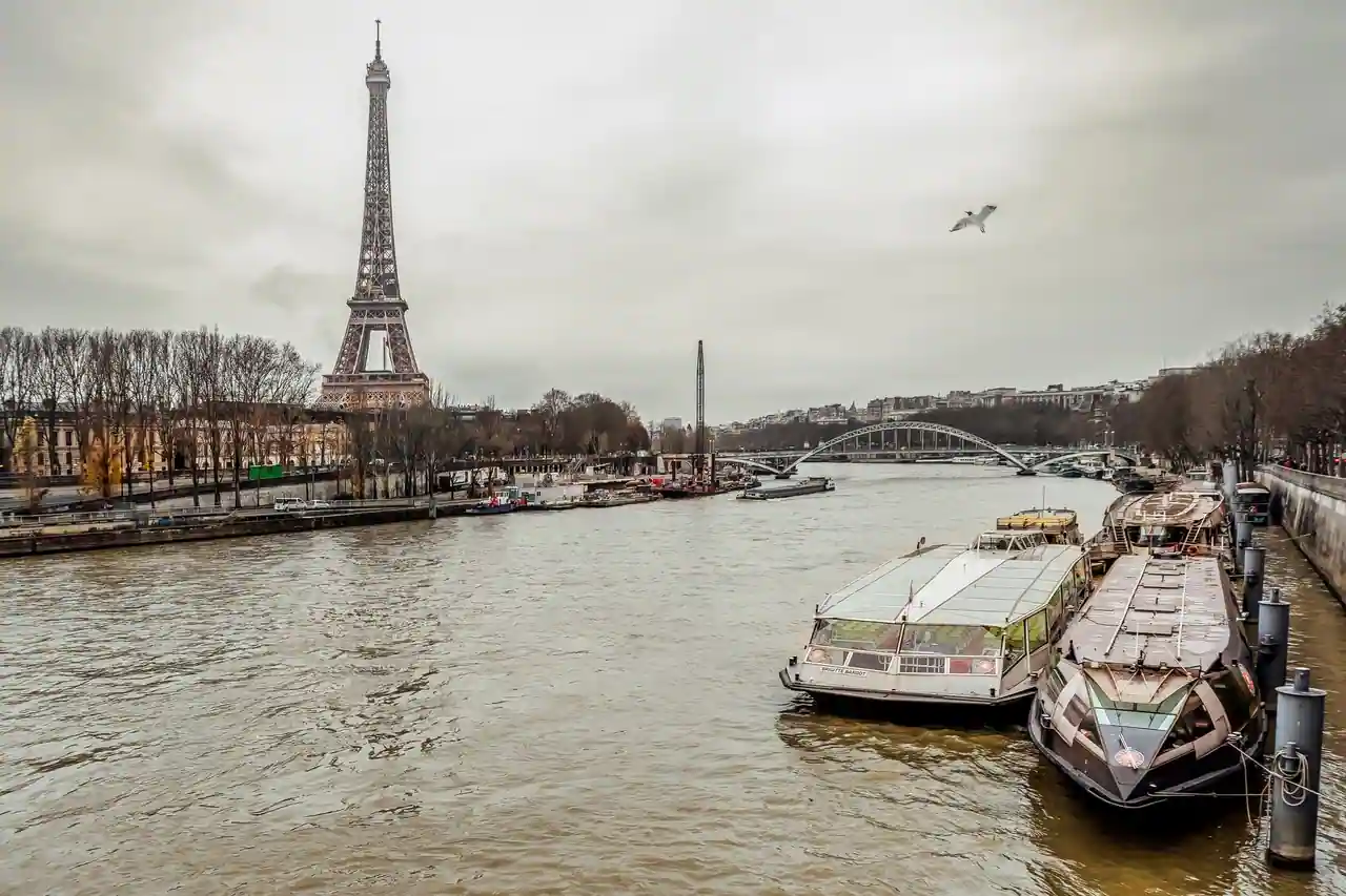Péniches amarrées le long d'un quai de la Seine à Paris, la tour Eiffel en arrière-plan sous un ciel gris.