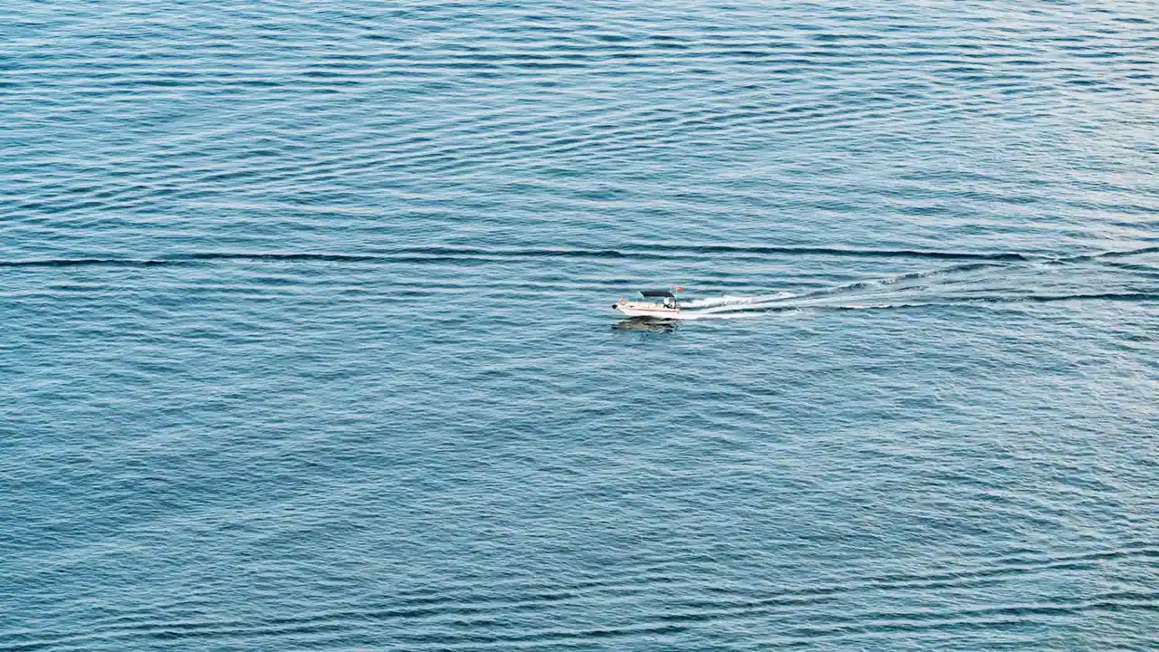 Un petit bateau navigue sur une vaste étendue d'eau calme, laissant un léger sillage.