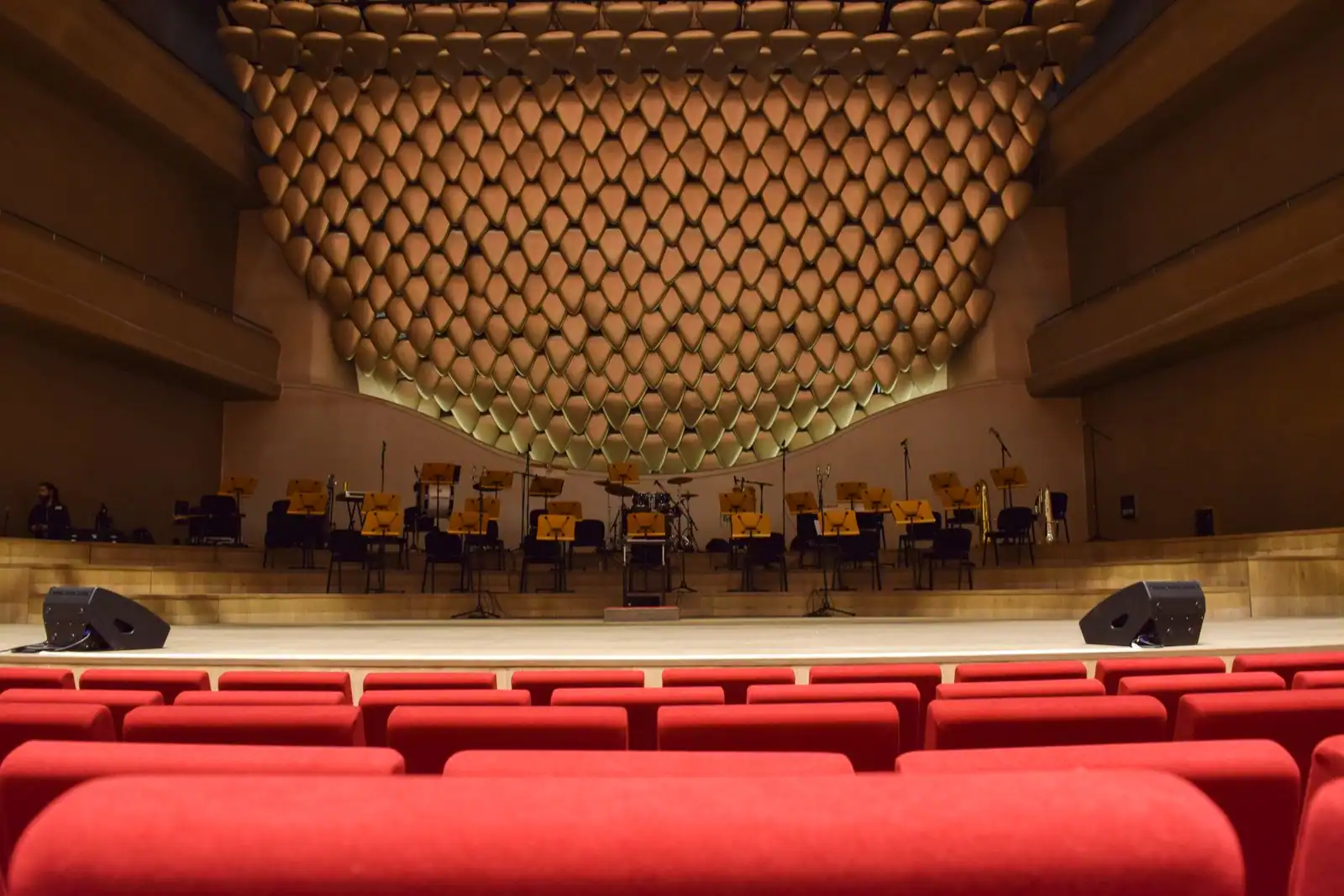 Intérieur d'une salle de concert avec des sièges rouges face à une scène et des pupitres de musiciens.