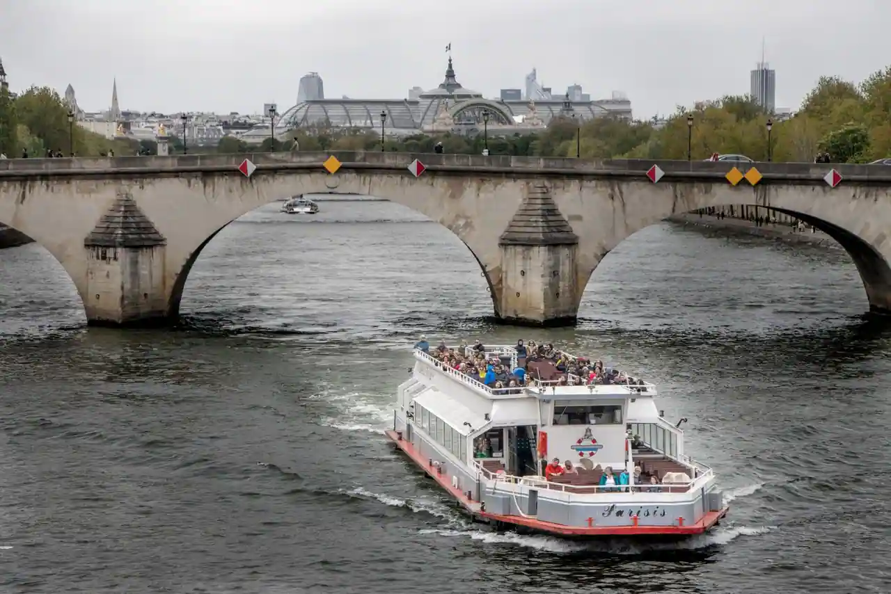 Bateau de promenade à pont découvert sur la Seine à Paris, devant un pont en pierre