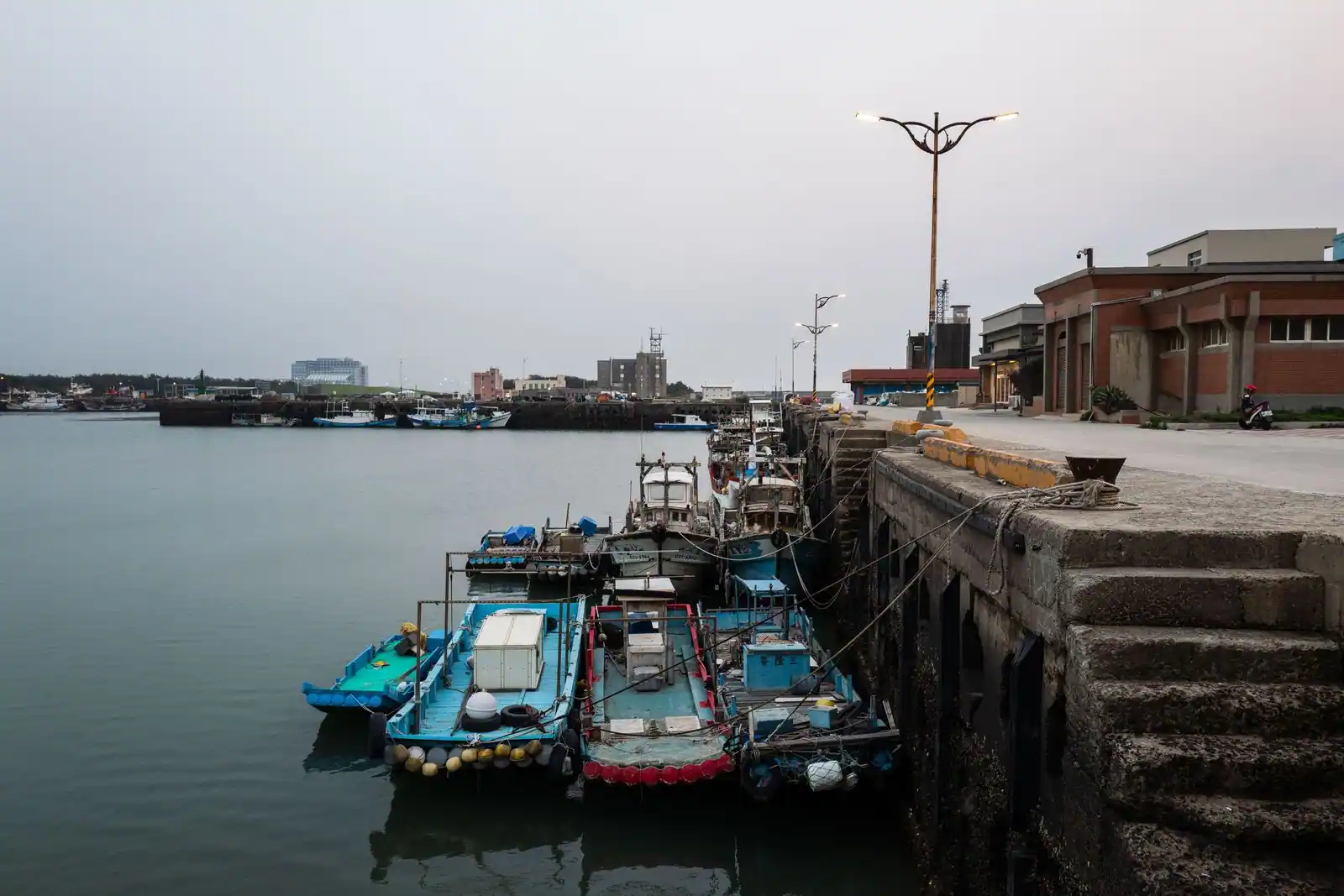 Bateaux de pêche amarrés le long d'un quai dans un port tranquille, sous une lumière douce.