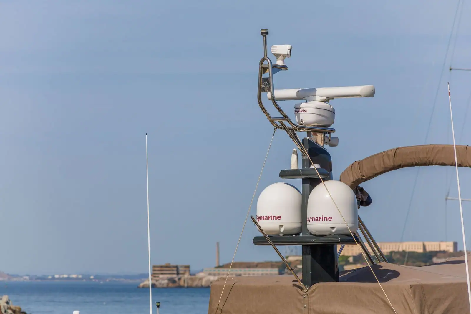 Équipement de navigation sur le portique d'un bateau : antenne radar à barre et dômes blancs, face à la mer.