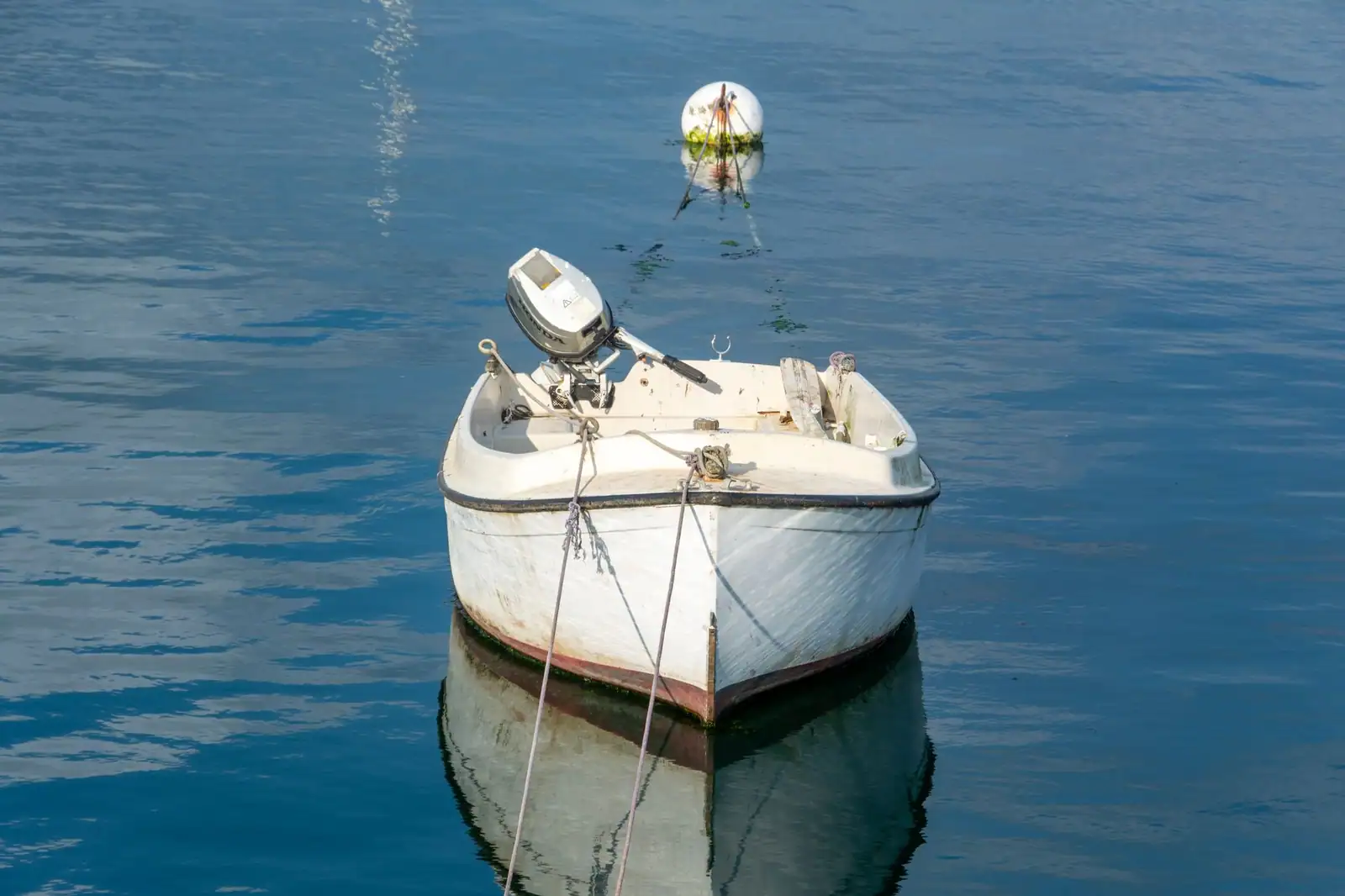 Petit bateau à moteur hors-bord amarré sur une eau calme et bleue par beau temps