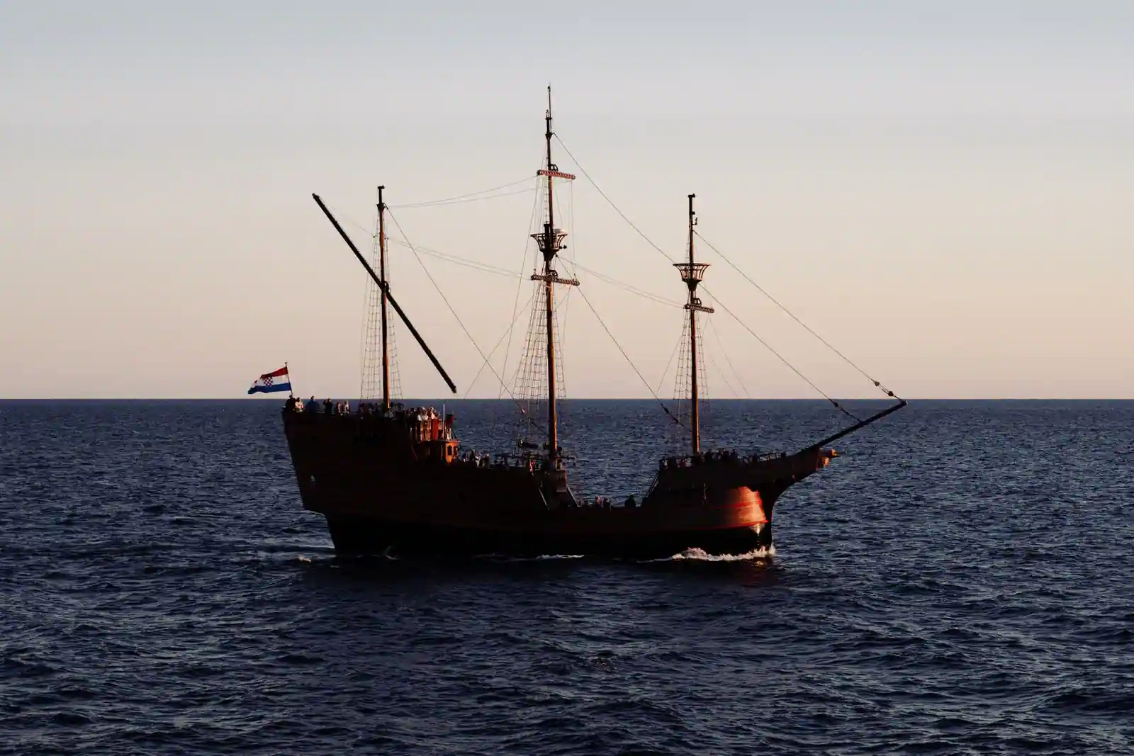 Réplique d'un ancien navire en bois à trois mâts naviguant sur une mer calme au crépuscule