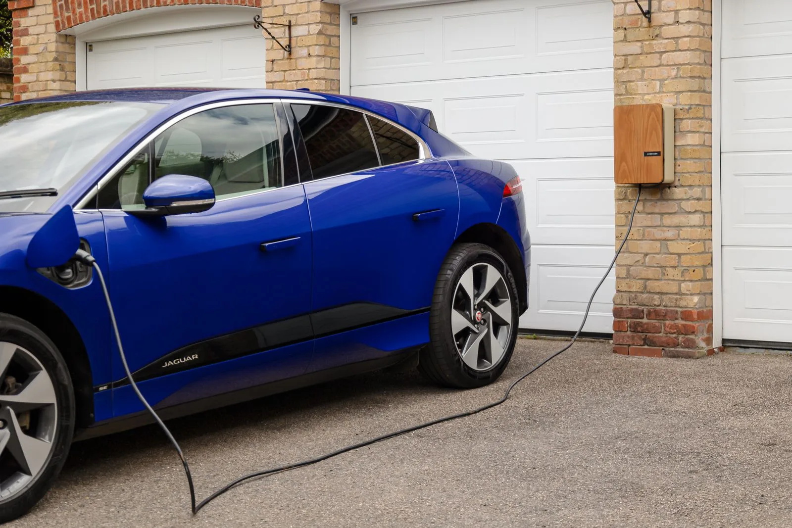 Voiture électrique bleue branchée à une borne de recharge murale devant un garage.