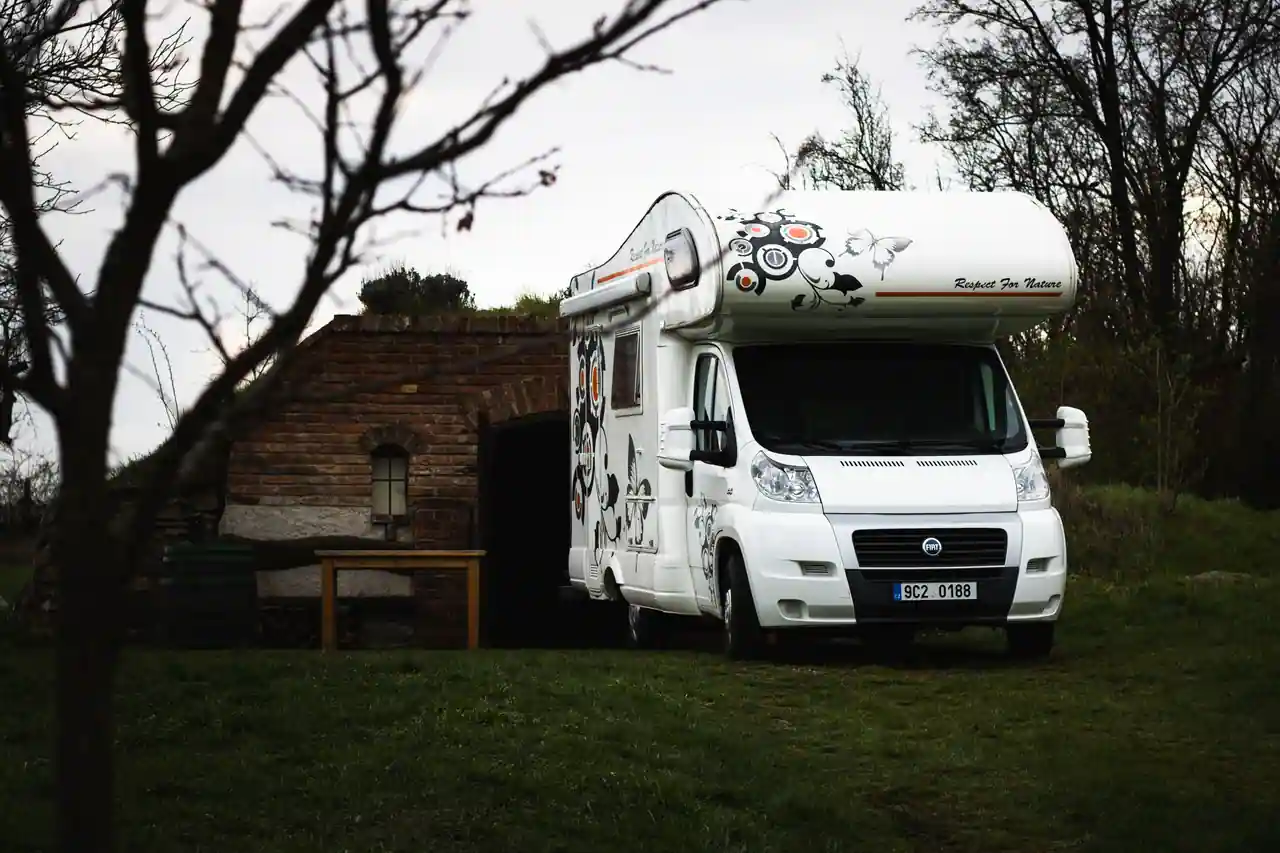 Camping-car stationné en extérieur sur un terrain herbeux, à l'écart d'un bâtiment ancien