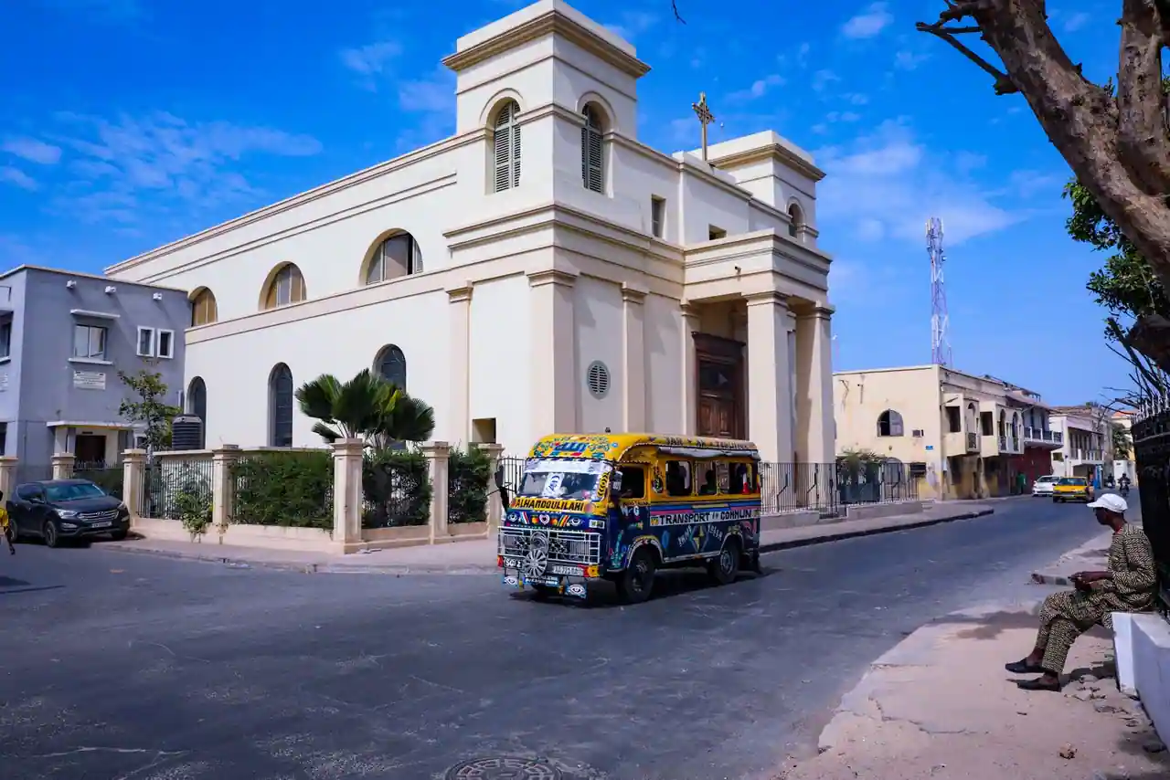 Car rapide aux couleurs vives, minibus de transport en commun typique de Dakar, passant devant une église de la ville