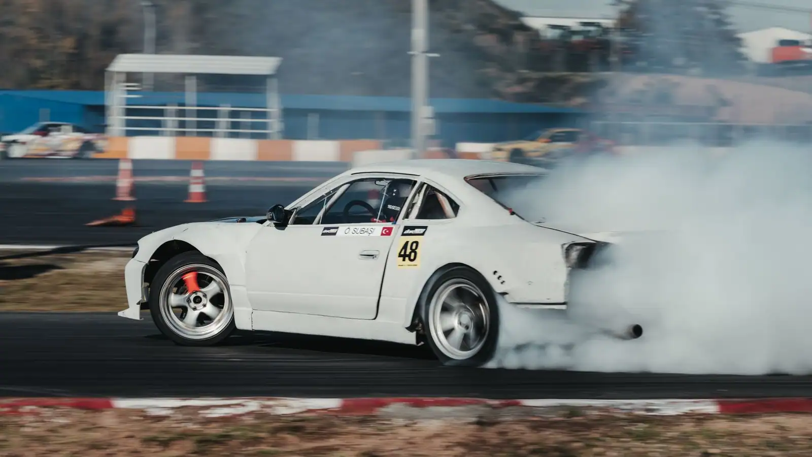 Voiture de course blanche de profil en plein drift, fumée de pneus à l'arrière sur un circuit.