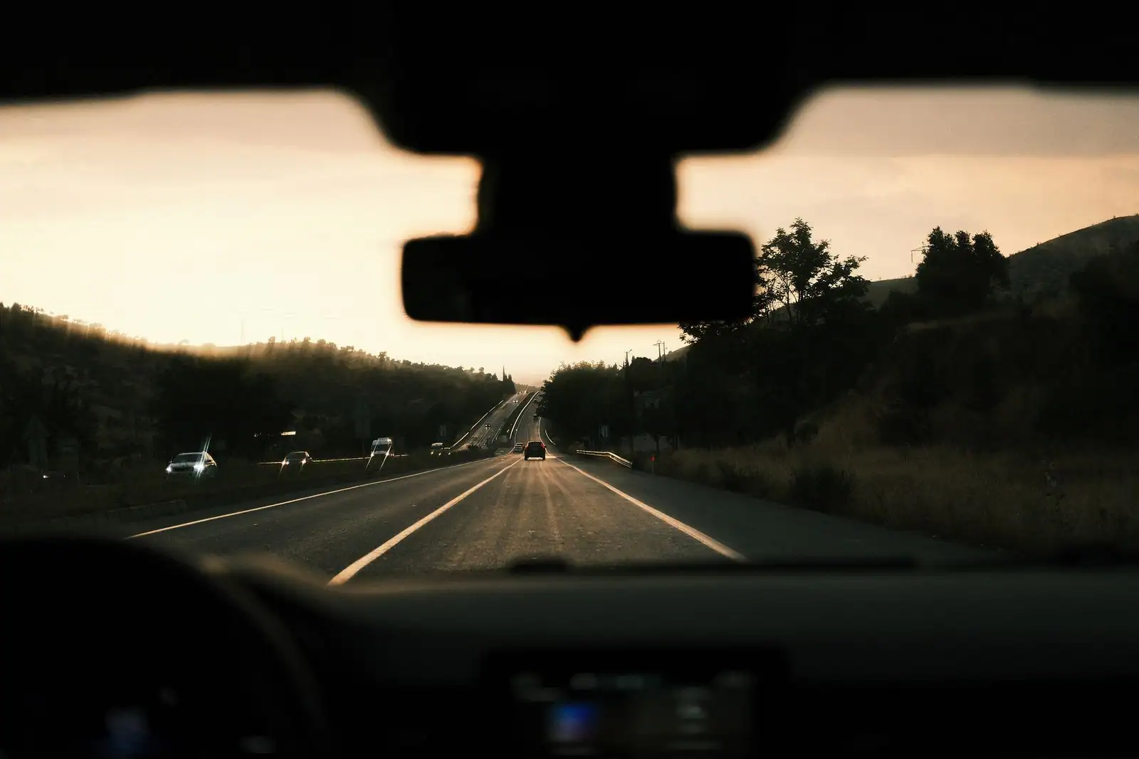 Vue de la route à travers le pare-brise d'une voiture en mouvement, au crépuscule, tableau de bord au premier plan.