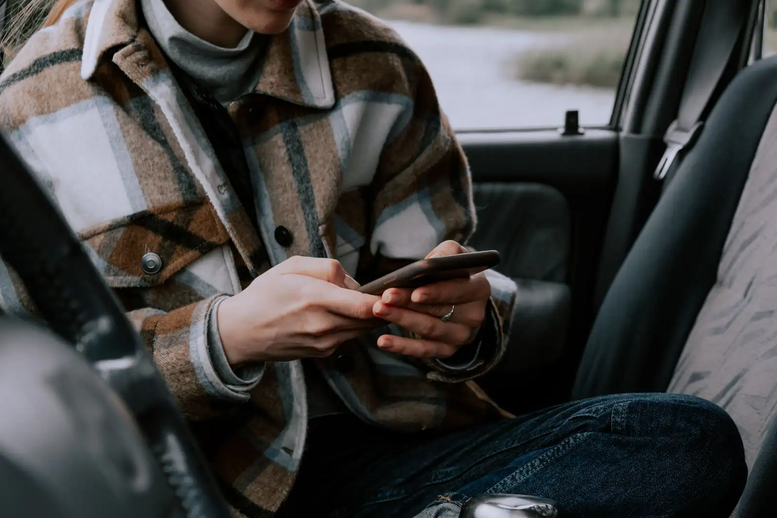 Personne assise dans une voiture tenant un smartphone à deux mains, volant visible à gauche