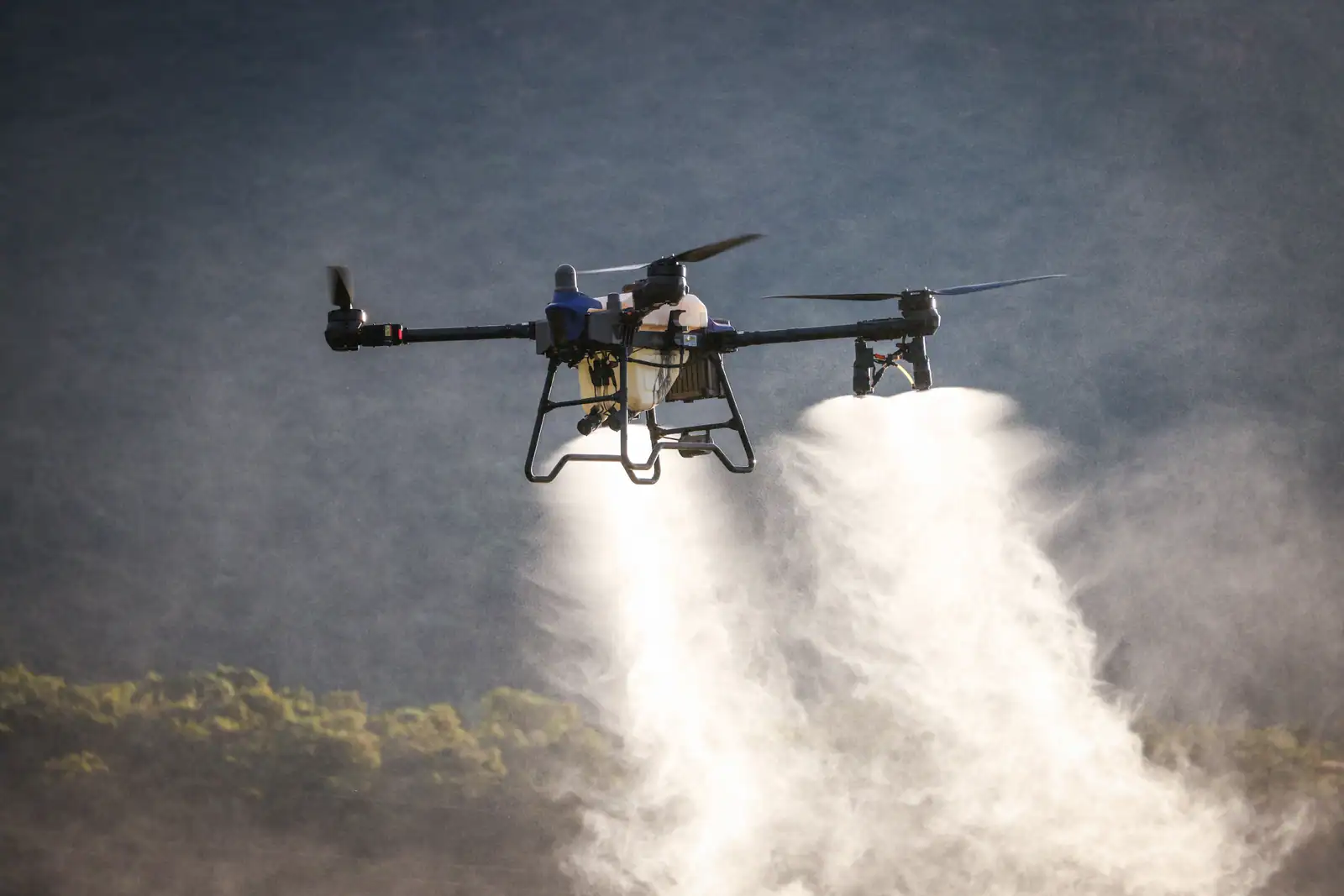 Drone professionnel multirotor à réservoir en vol, en train d'épandre au-dessus d'une parcelle