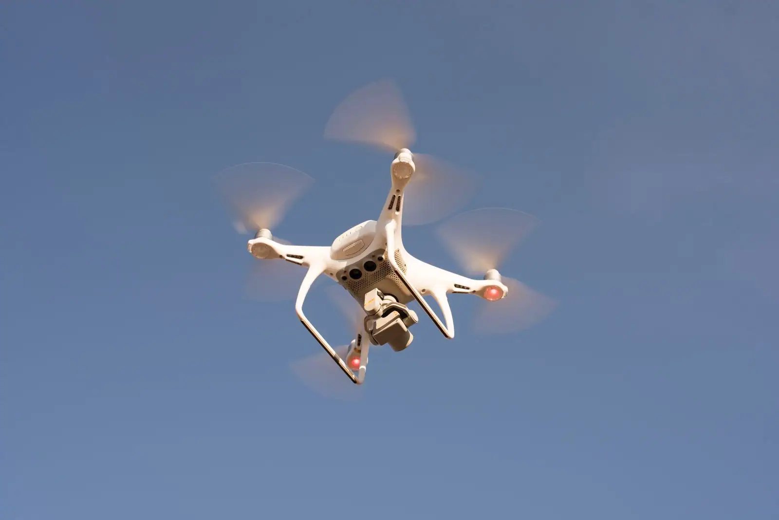 Drone quadricoptère en vol stationnaire dans un ciel dégagé, vu en légère contre-plongée.