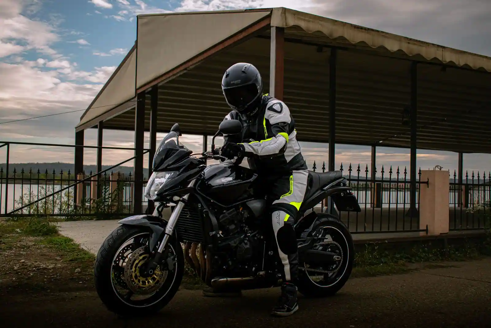 Motard en équipement complet — casque, blouson et gants de protection — installé sur sa moto au bord de l'eau