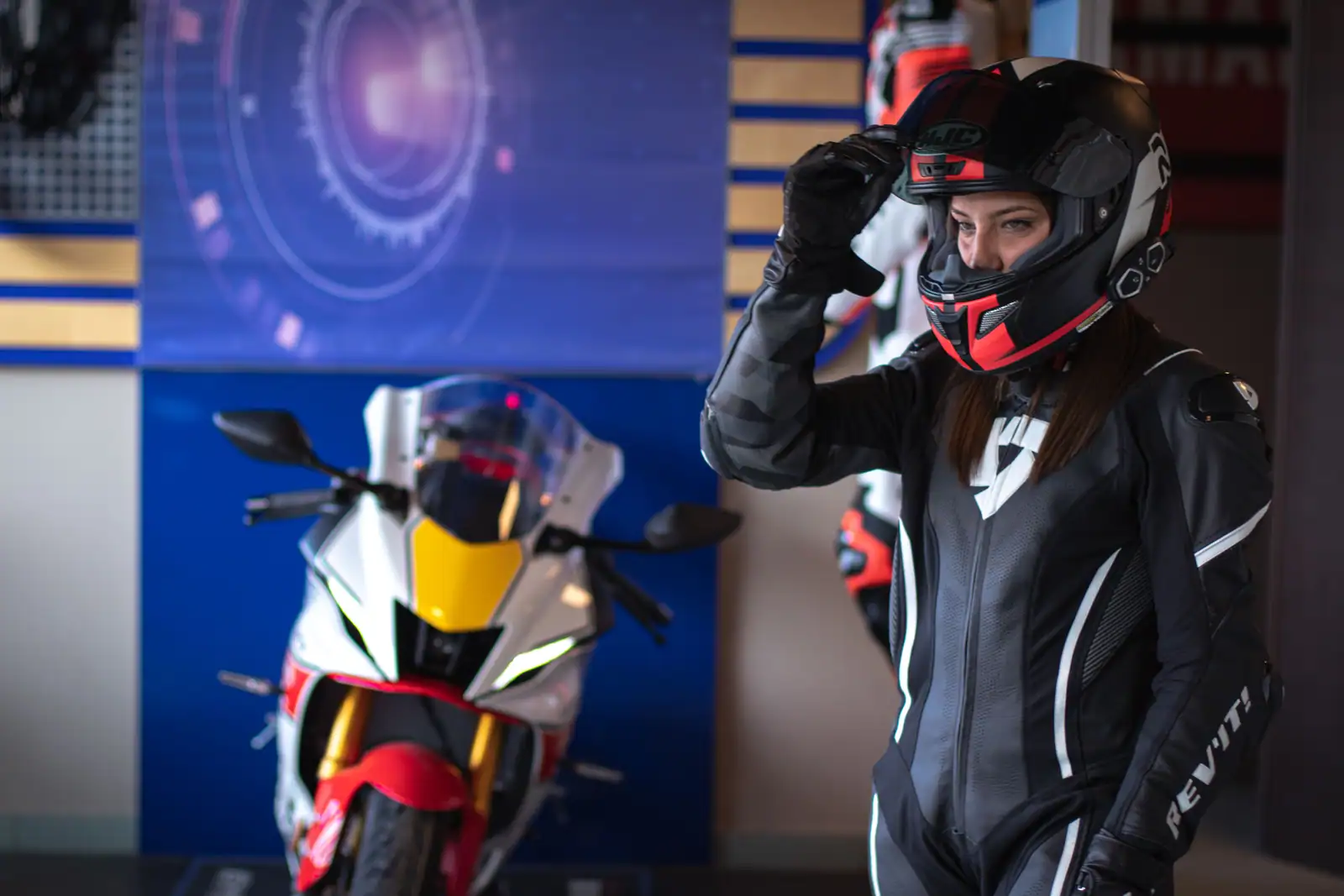 Motarde en combinaison de cuir ajustant son casque intégral, moto sportive en arrière-plan