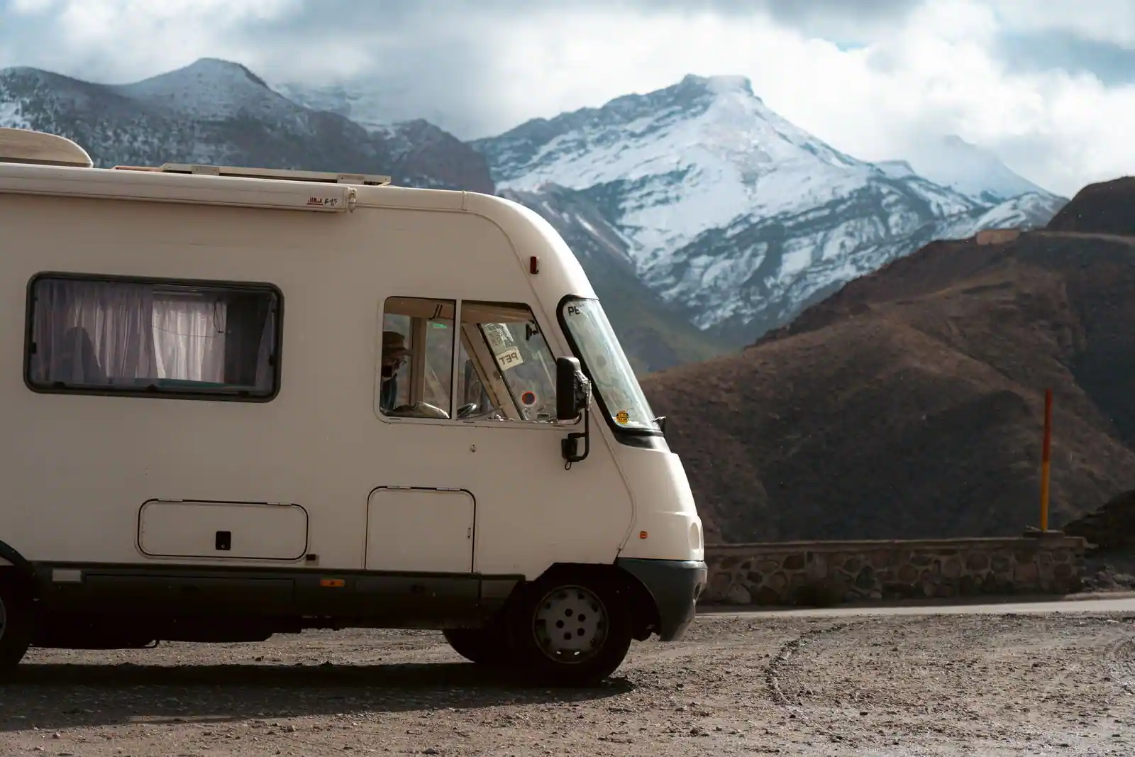 Camping-car blanc de profil stationné devant des montagnes enneigées sous un ciel nuageux