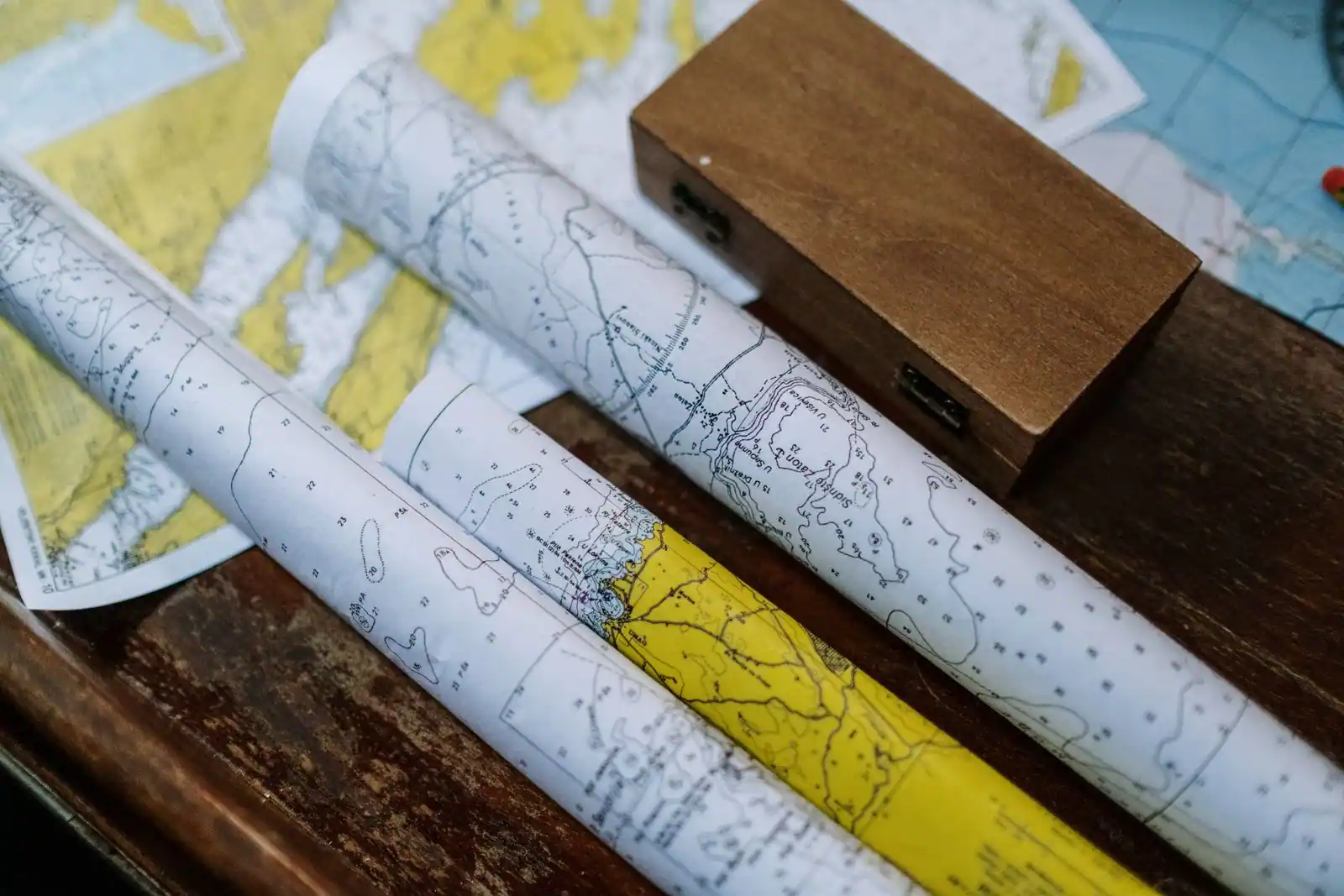 Cartes marines enroulées posées sur une table en bois près d'une boîte d'instruments de navigation