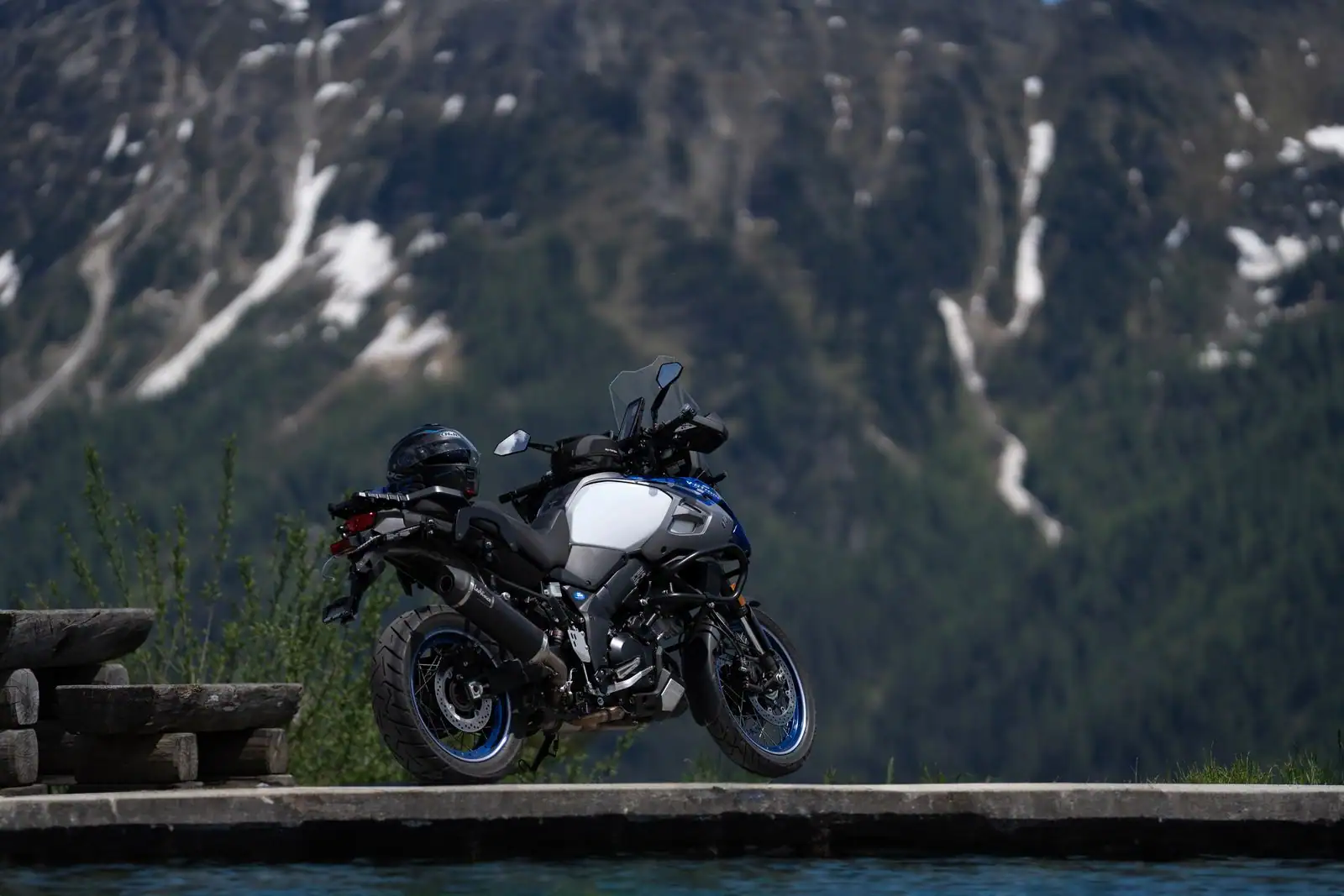 Moto trail d'aventure à l'arrêt devant un paysage de montagne enneigée, casque posé sur la selle.