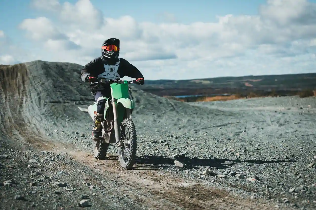 Pilote en équipement sur une moto tout-terrain franchissant un terrain caillouteux à découvert.