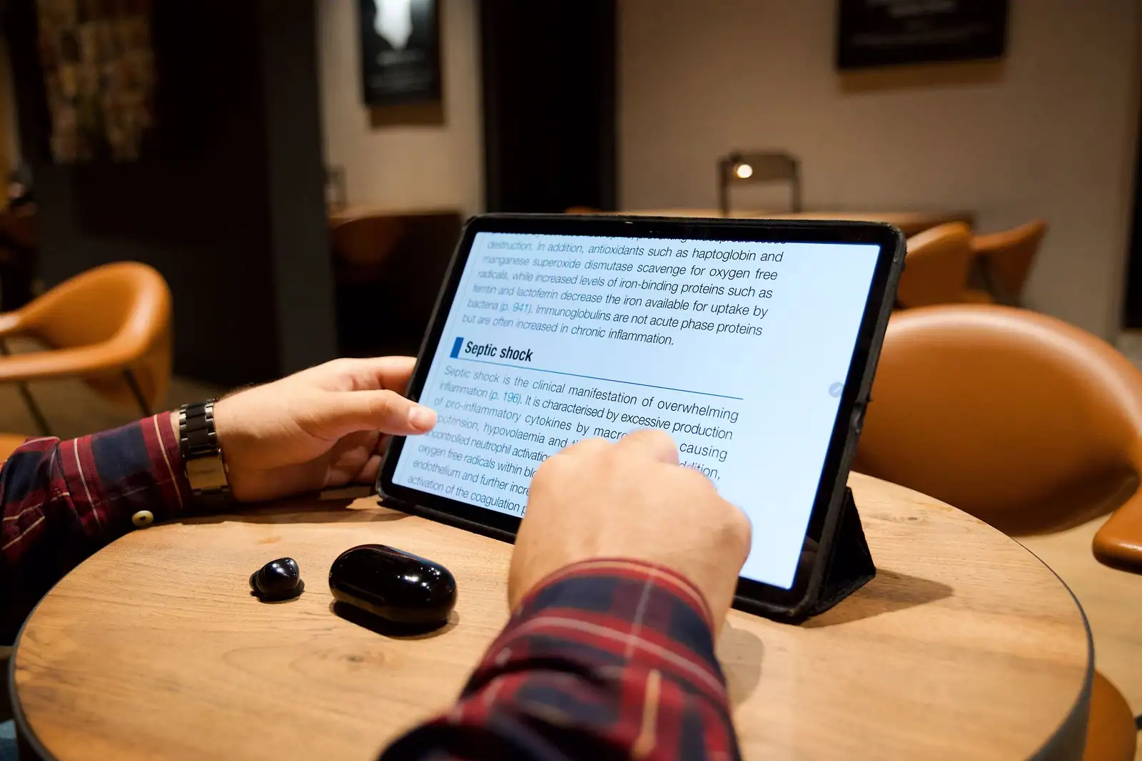 Une personne lit un texte sur une tablette posée sur une table en bois, dans un intérieur chaleureux et tamisé.