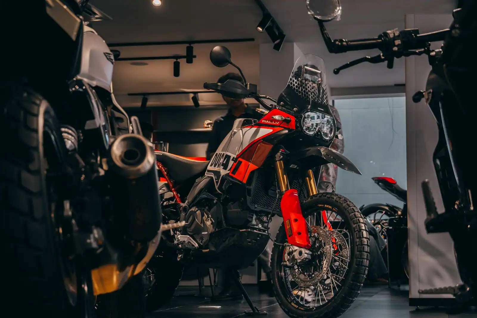 Moto trail moderne exposée dans un showroom, vue de trois quarts avant, d'autres motos autour.