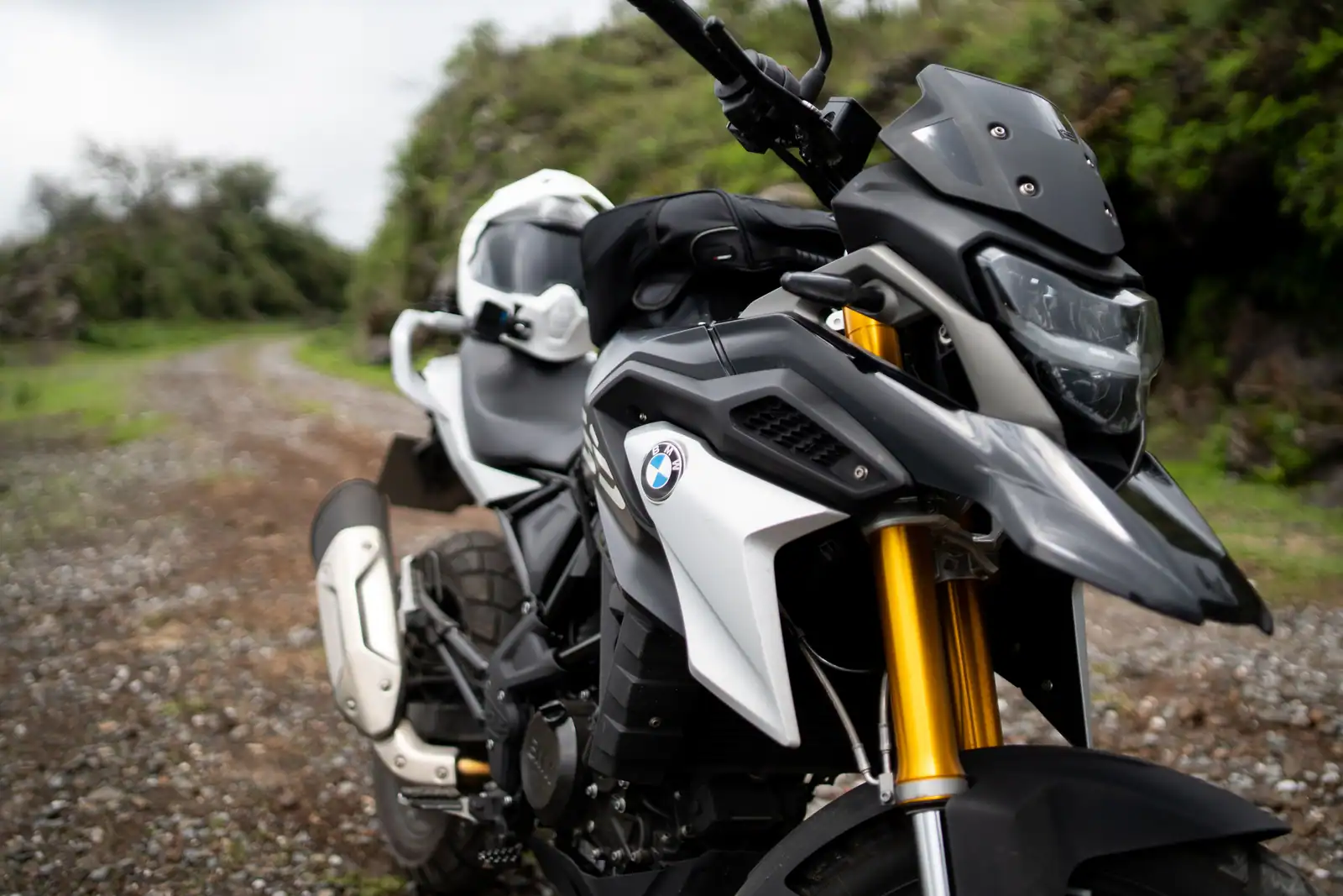Moto d'aventure BMW GS sur un chemin de gravier, fourche inversée dorée et bec caractéristique de la famille GS