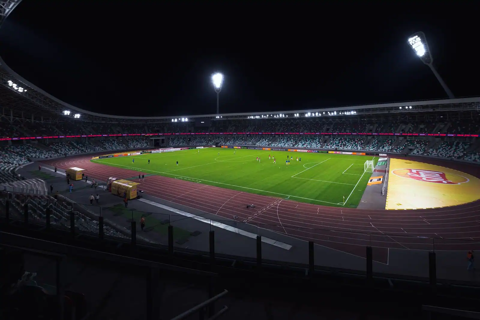 Stade de football illuminé la nuit sous les projecteurs, vu depuis les tribunes.
