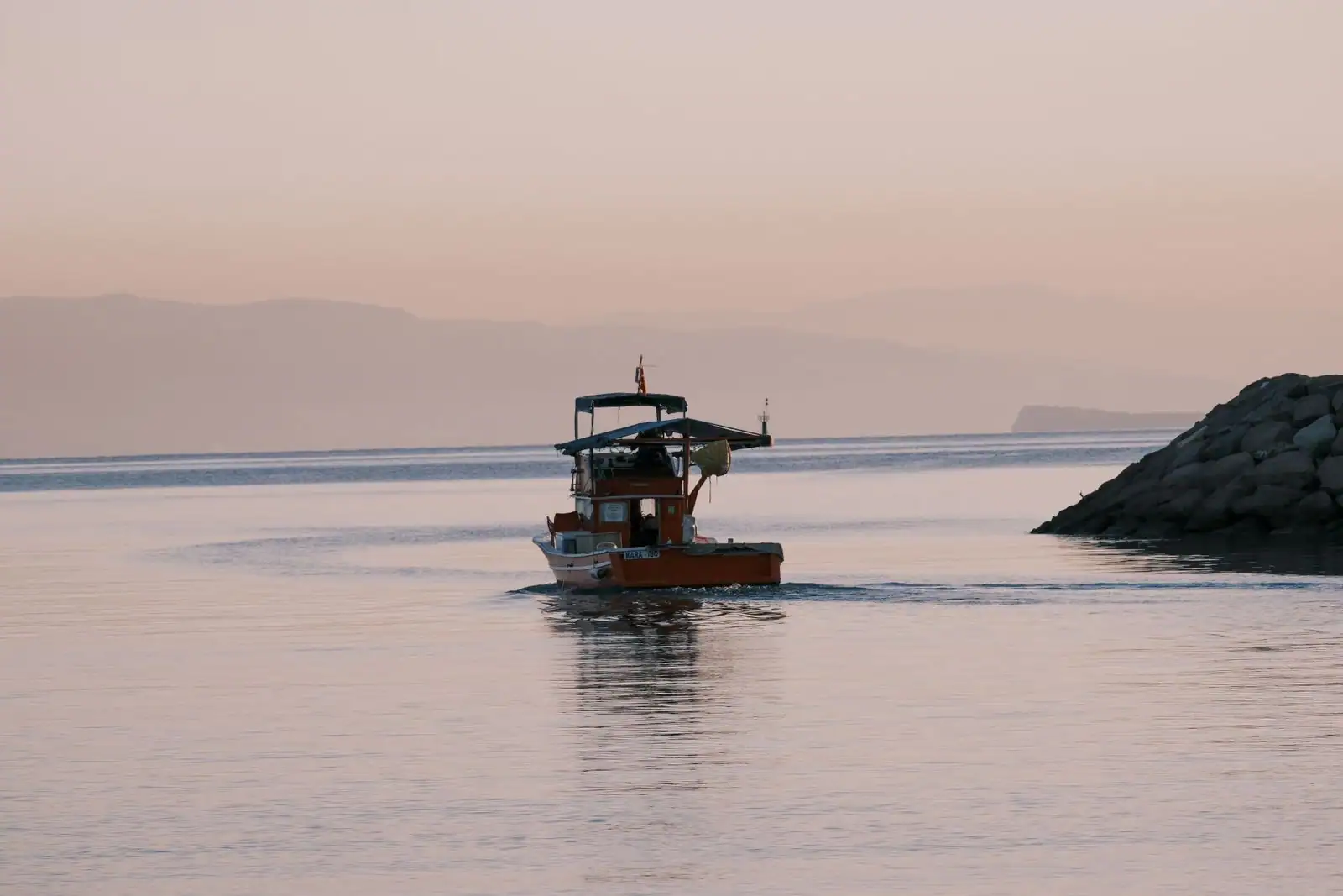 Petit bateau à moteur navigant sur une eau calme près d'un môle rocheux à la lumière du crépuscule