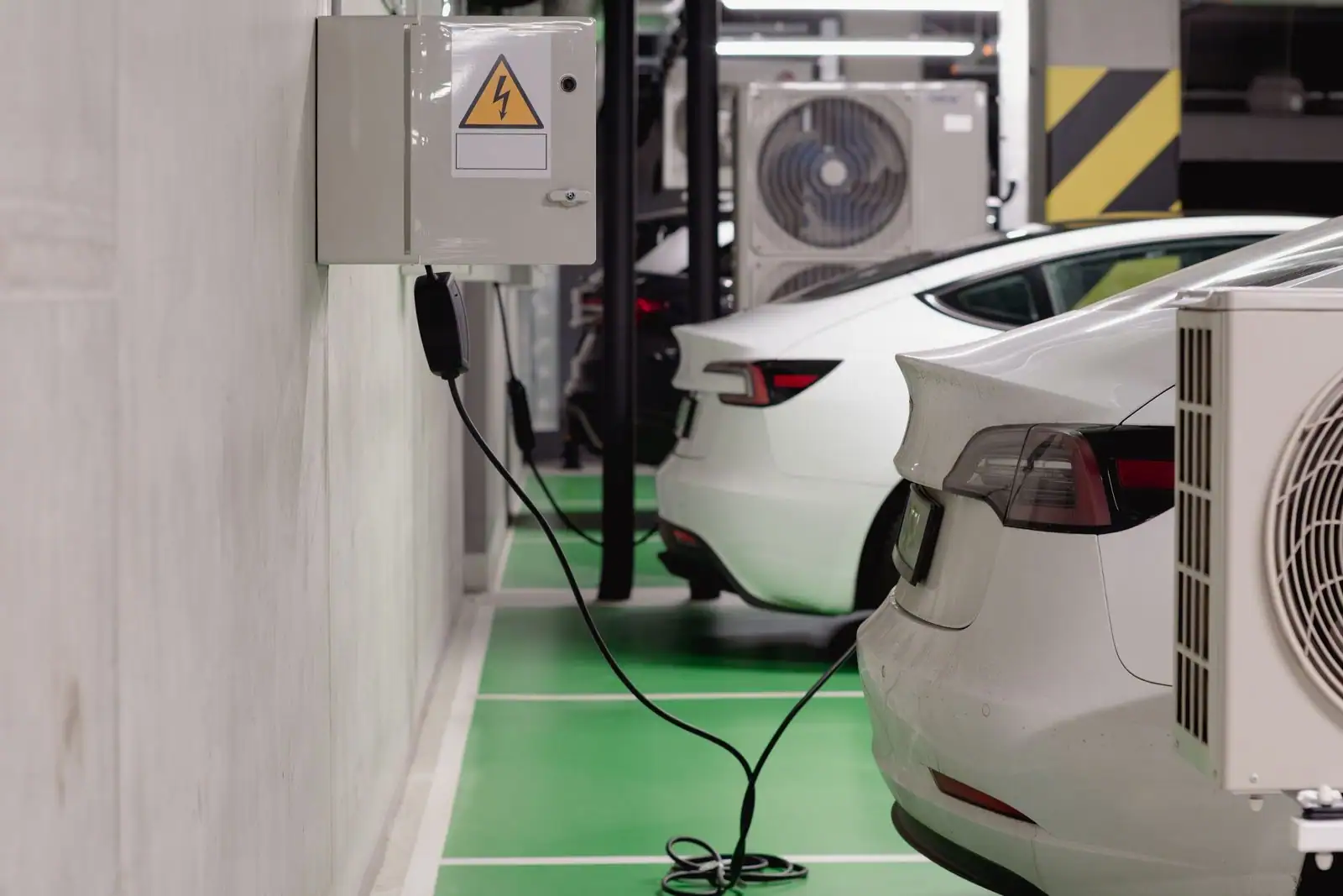 Voitures électriques blanches branchées à une borne de recharge murale sur une place de parking