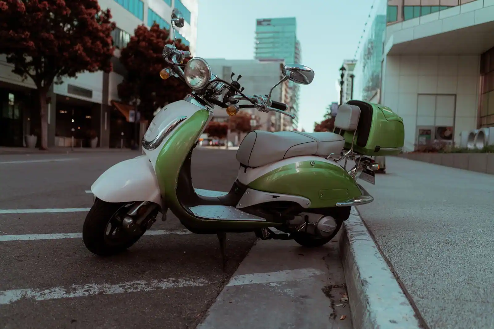Un scooter rétro vert et blanc stationné le long d'un trottoir, dans une rue de ville.