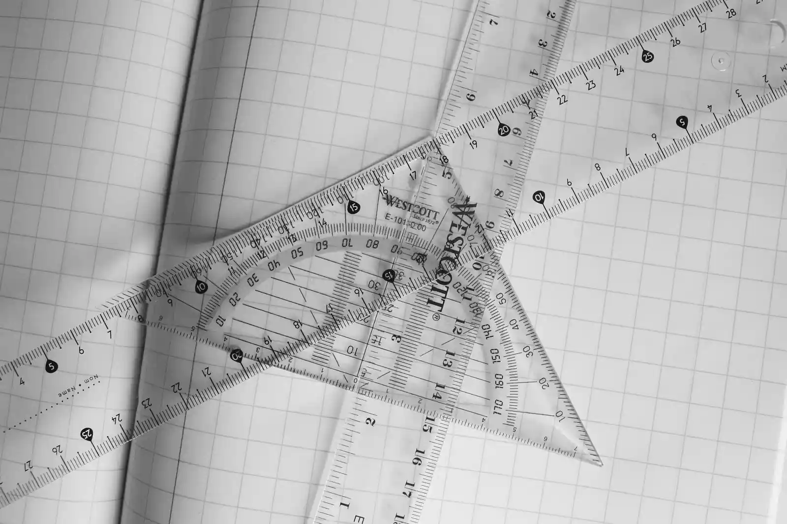 Règles graduées et équerre transparentes posées sur une feuille de papier quadrillé