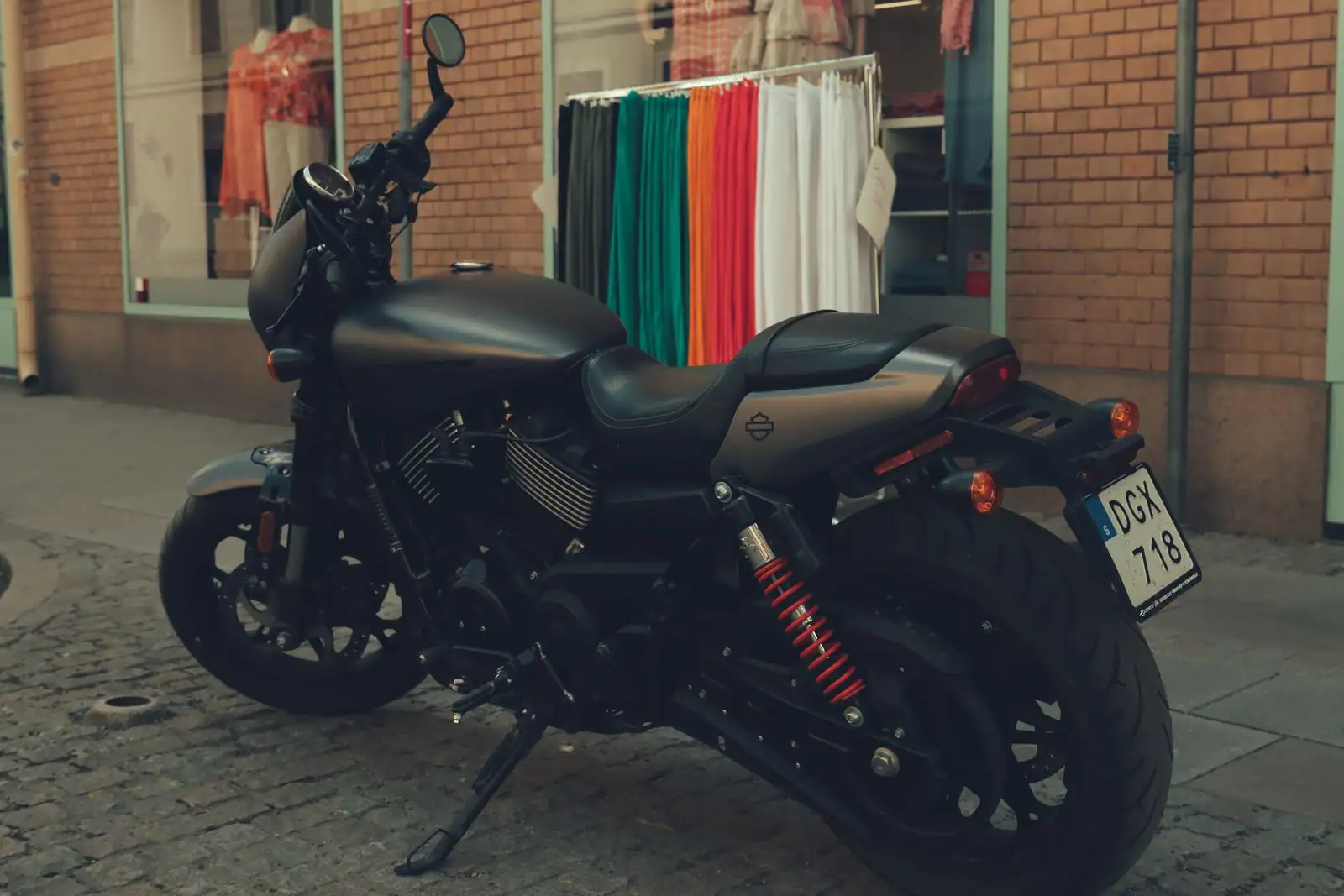 Moto nue à la robe sombre stationnée dans une rue pavée, devant la vitrine d'une boutique.