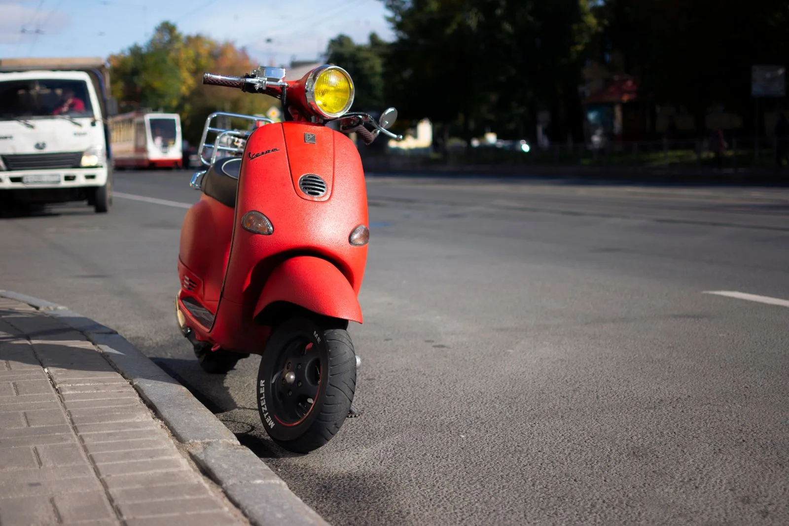 Scooter rouge de style urbain stationné le long d'un trottoir, vu de trois quarts avant