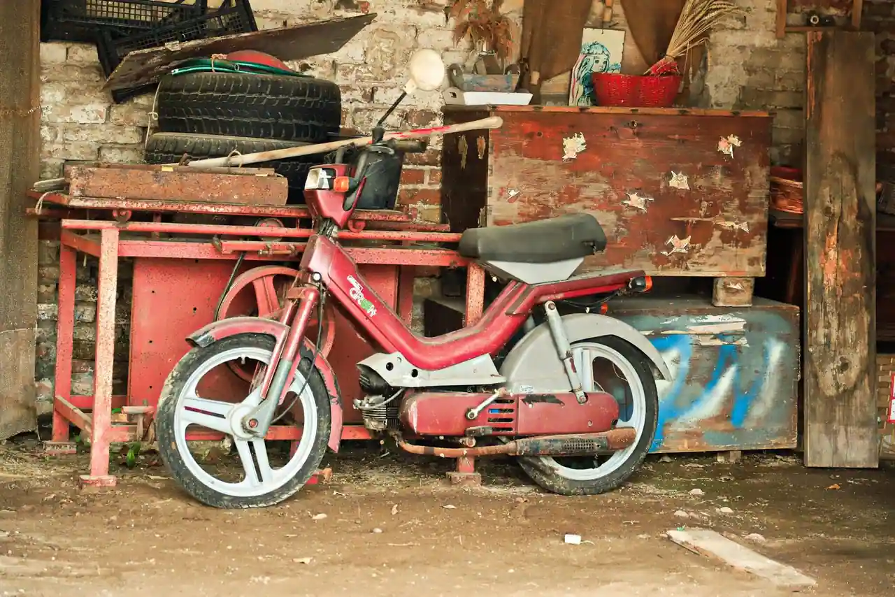 Vieux cyclomoteur garé dans un atelier encombré, évoquant l'entretien d'un deux-roues motorisé