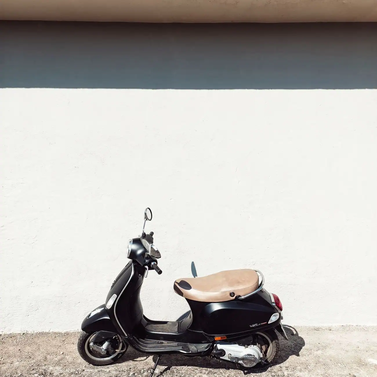 Scooter urbain garé le long d'un mur blanc ensoleillé, composition épurée et illustrative.