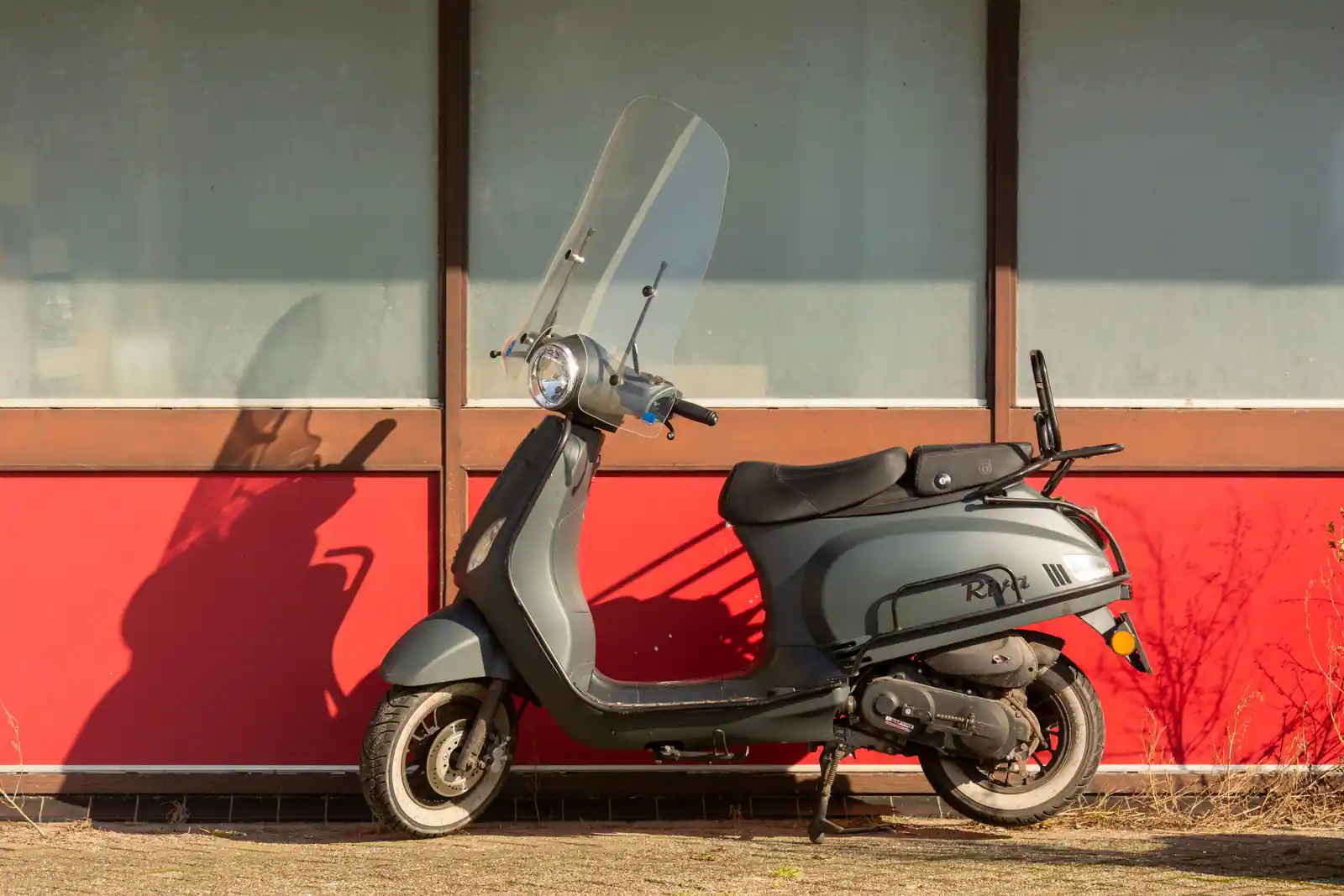 Scooter gris à pare-brise stationné de profil le long d'un mur en ville