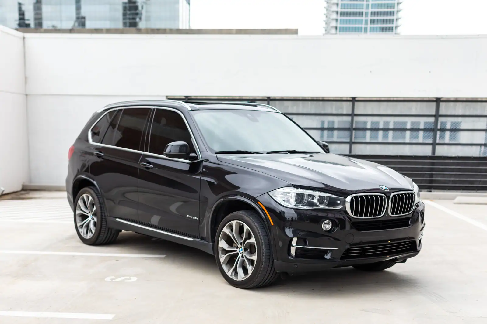 SUV de luxe noir vu de trois quarts avant sur un parking urbain en hauteur