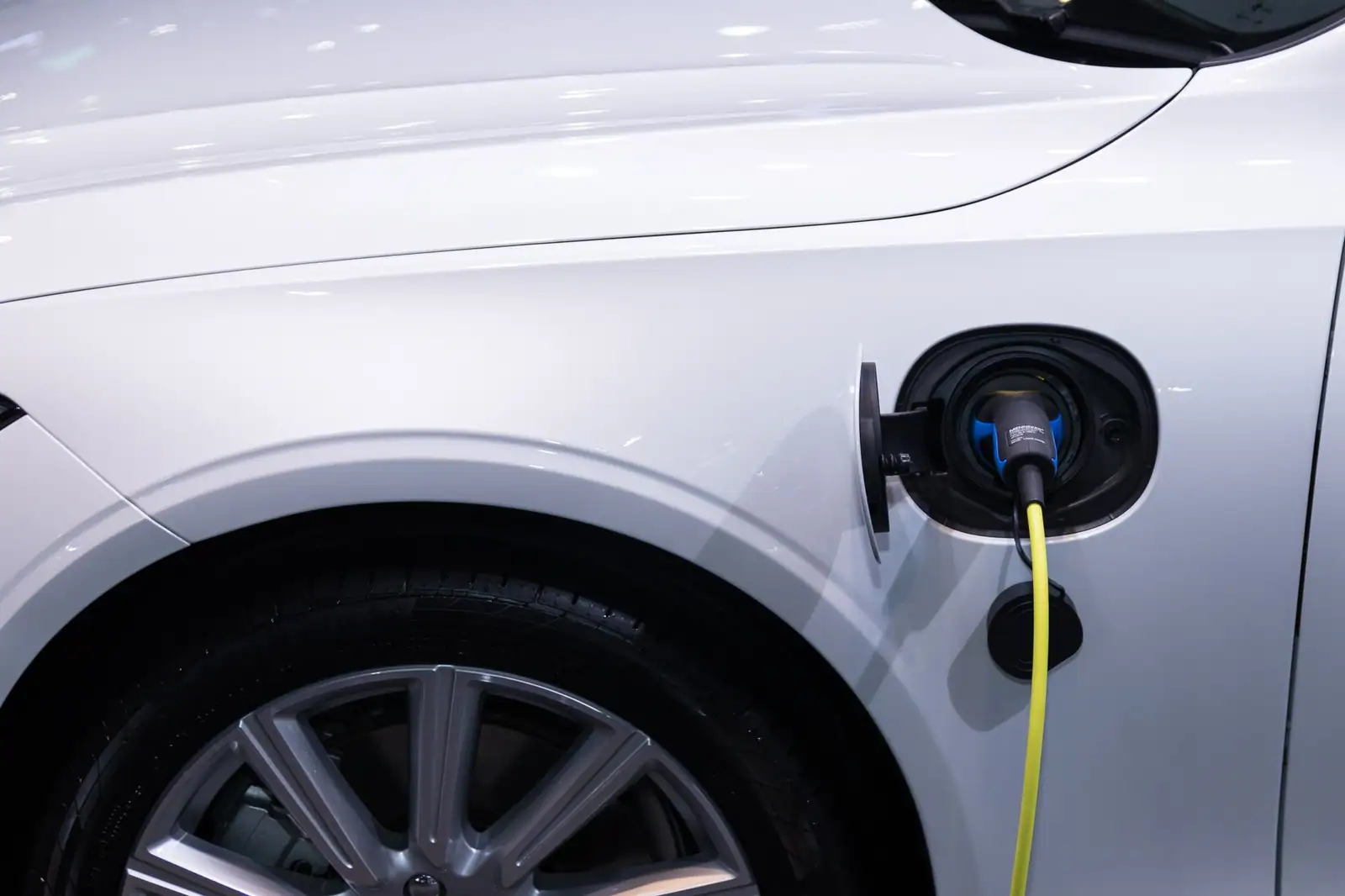 Voiture électrique blanche en charge, câble jaune branché sur la trappe latérale, jante visible.