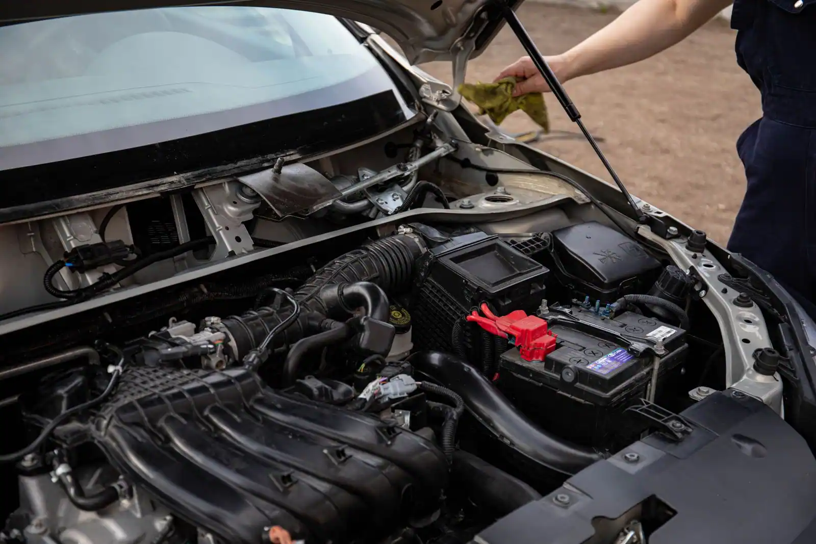 Compartiment moteur ouvert d'une voiture, batterie visible, une personne penchée sous le capot