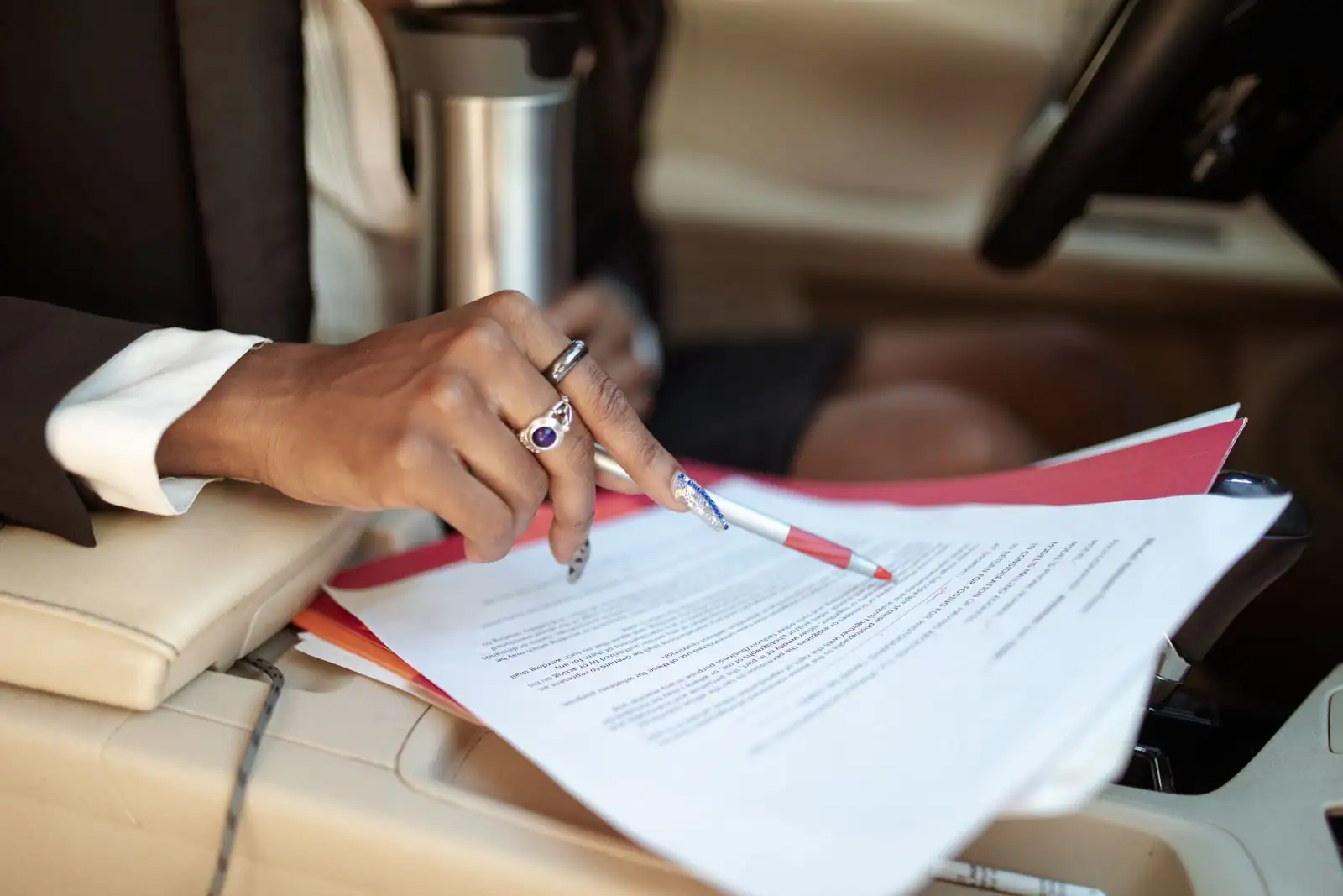 Personne annotant un document administratif au stylo, dans l'habitacle d'une voiture.
