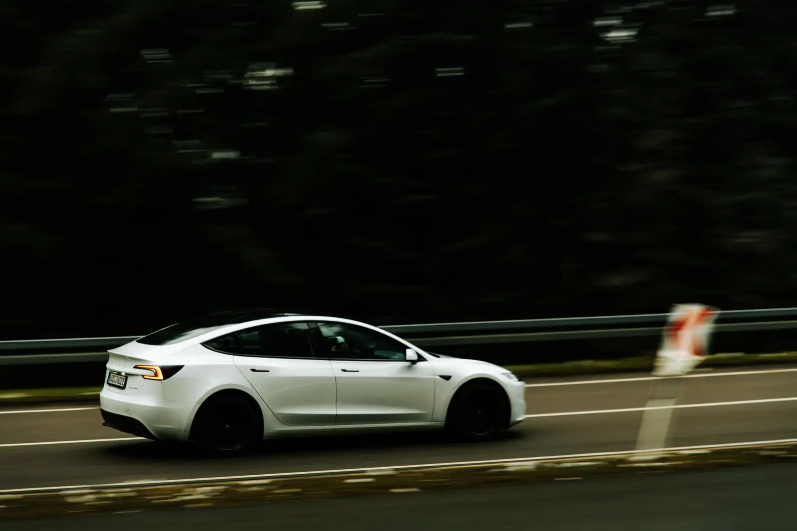 Une voiture électrique moderne blanche roulant sur une route, vue de profil en mouvement