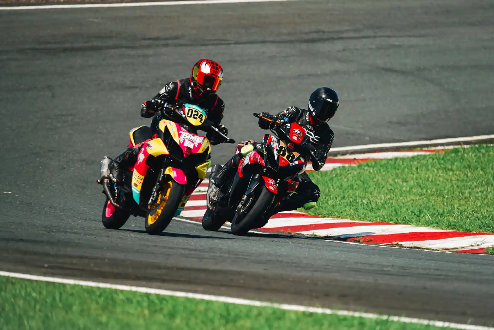 Deux pilotes numérotés côte à côte, inclinés dans le même virage sur un circuit moto.
