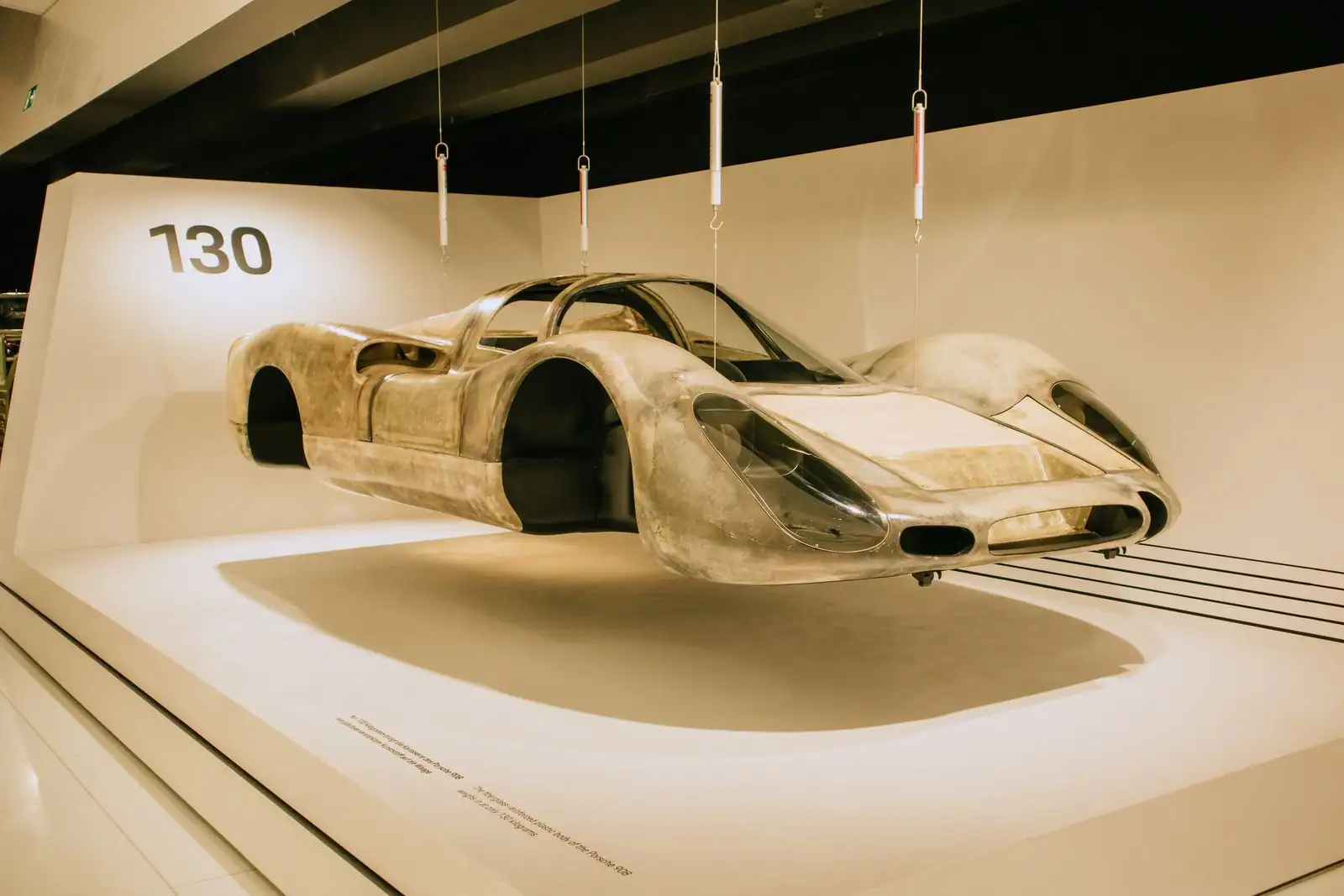 Carrosserie nue de voiture de course suspendue et éclairée dans une salle de musée, comme une sculpture