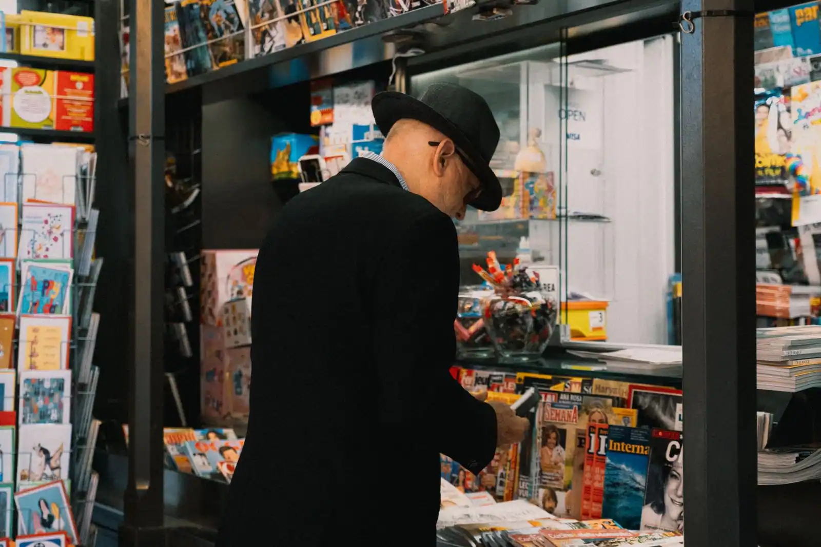 Un homme feuillette une publication devant les présentoirs bien garnis d’un kiosque à journaux