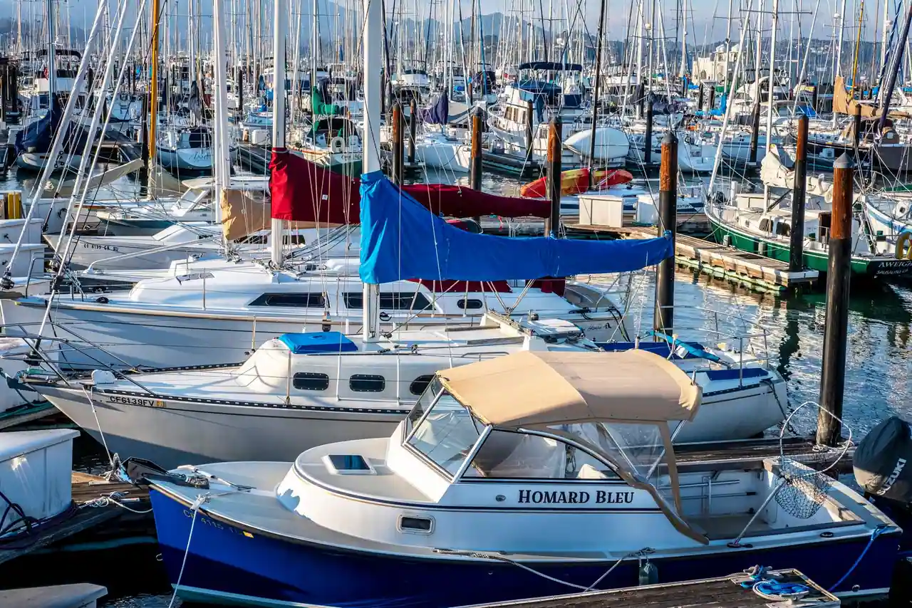 Voiliers et vedettes de plaisance amarrés côte à côte dans un port, mâts et tauds au premier plan