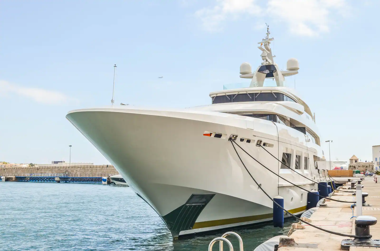 Grand yacht à moteur blanc amarré le long d'un quai, vu depuis la proue, par temps clair.