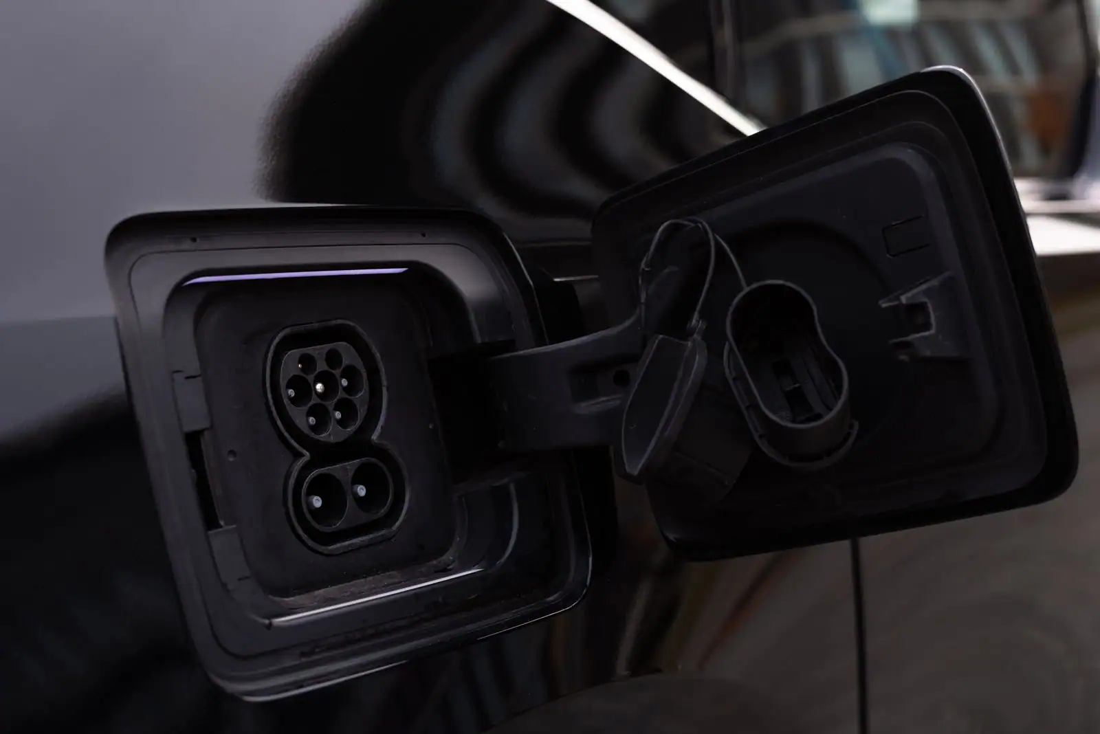 Trappe de charge ouverte sur la carrosserie sombre d'une voiture électrique, prise apparente